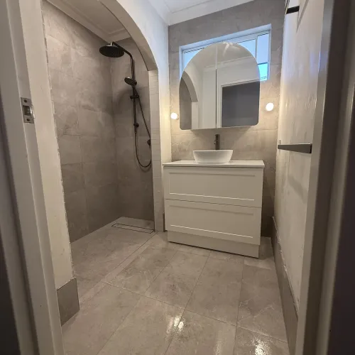 Bathroom renovation with an arched shower doorway, floating vanity and round mirror