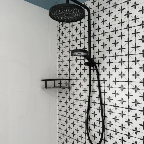 Close-up of a black rain shower head against patterned black-and-white tiling
