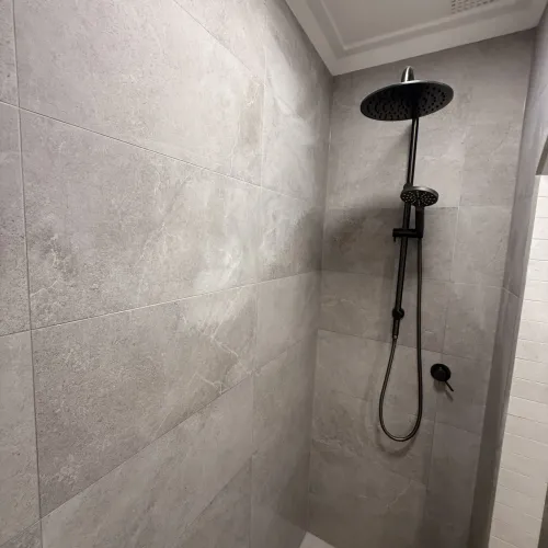 Close-up of a black rain shower head against light stone tiling