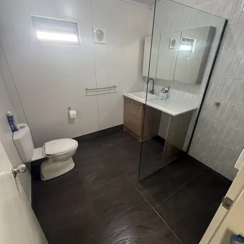 Bathroom renovation with a glass shower divider, timber vanity and dark tile flooring