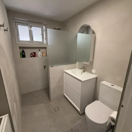Bathroom renovation with a frosted glass shower divider, arched mirror and cream tiling