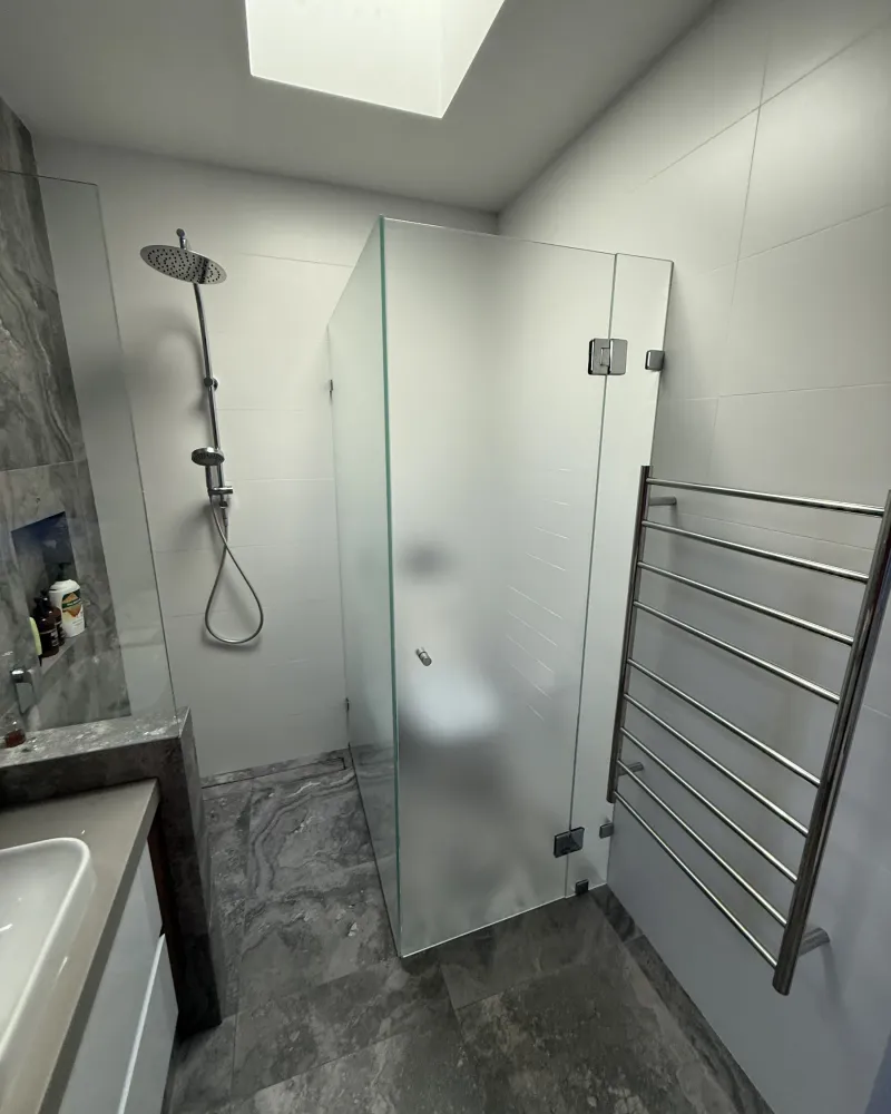 Walk-in shower renovation with a rain shower head, heated towel rail and grey stone tiling, completed by Integra Renovations