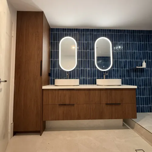 Bathroom renovation with dual vessel sinks, backlit oval mirrors and navy feature tiling