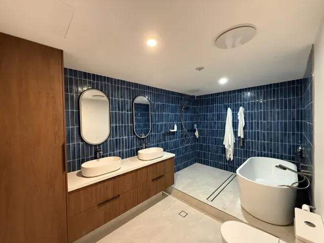 Premium bathroom renovation with a freestanding oval bath, dual backlit oval mirrors and navy feature tiling