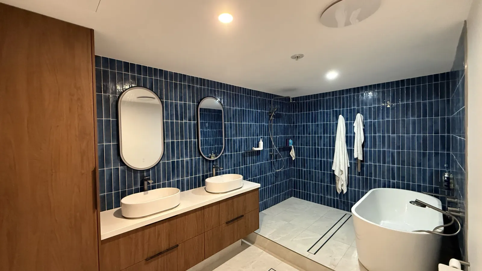 Bathroom renovation with a freestanding oval bath, dual backlit oval mirrors and navy feature tiling, completed by Integra Renovations