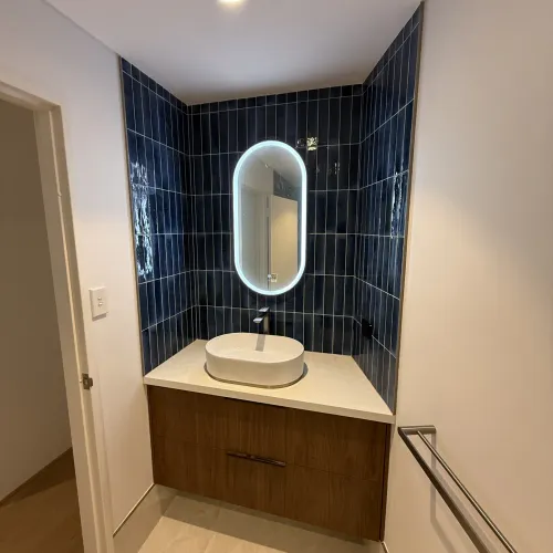 Powder room renovation with a pill-shaped backlit mirror and navy feature tiling