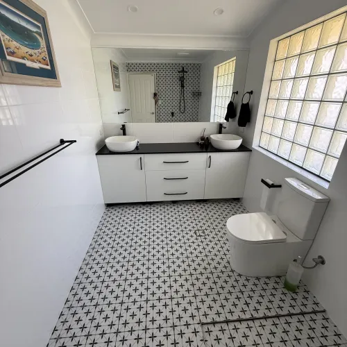 Bathroom renovation with dual vessel sinks, patterned tile flooring and a glass block window